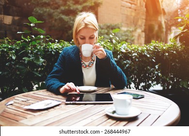 Young attractive businesswoman at coffee time working on digital tablet while sitting on the terrace of coffee shop, caucasian blond well dressed woman using touch pad while sitting in coffee shop - Powered by Shutterstock