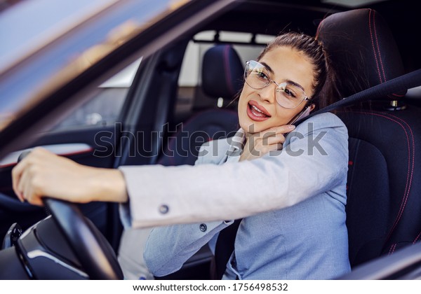 Young attractive businesswoman dressed smart\
causal sitting in her car, driving it and using smart phone. Unsafe\
drive concept.