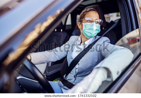 Young attractive\
businesswoman dressed smart casual with protective mask and gloves\
on sitting in her car and she is ready to drive it. Protection from\
corona virus concept.