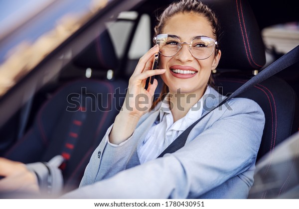Young attractive businesswoman dressed smart\
causal sitting in her car, driving it and using smart phone. Unsafe\
drive concept.