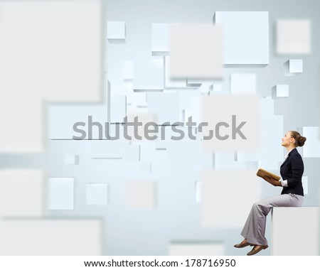 Young attractive businesswoman sitting on white cube and reading