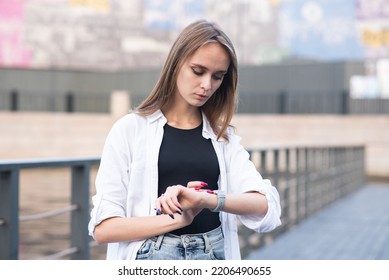 A young and attractive Caucasian girl in casual clothes looks at her wristwatch while walking.