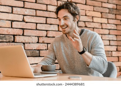 Young attractive caucasian man talking online using laptop against brick wall. Freelancer businessman tutor listening educational training course, seminar webinar, working remotely