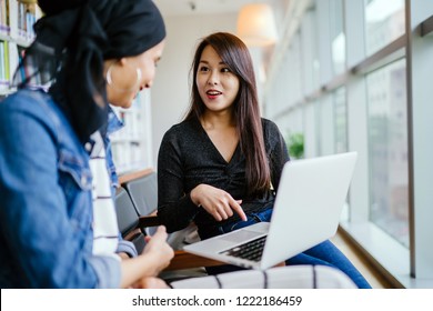 A Young And Attractive Chinese Asian Woman Has A Business Meeting With A Malay Muslim Woman. They Are Both Sitting In An Office And Talking Over A Laptop Computer During The Day. 