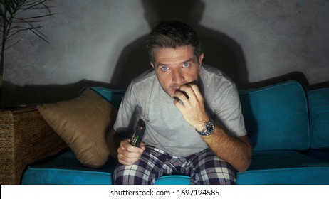 Young Attractive Concentrated And Scared Man Holding TV Remote Watching Horror Movie Or Suspense Thriller At Night In Home Couch Enjoying Film Emotion In Domestic Entertainment Concept