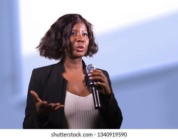 young attractive and confident black African American business woman with microphone speaking in auditorium at corporate event or seminar giving motivation and success coaching conference