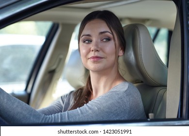 Young attractive coquettish caucasian woman in car flirting with pedestrian or other driver. Trendy and confident diverse woma behind the wheel. Pretty face expression, copy space.