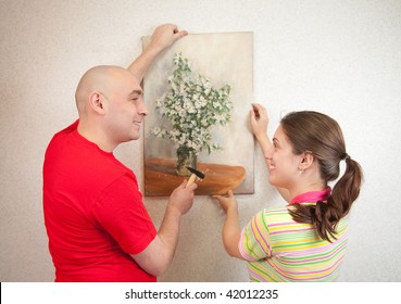 A Young And Attractive Couple Hanging Up An Art Picture On Their Wall