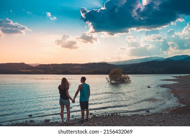 Young Attractive Couple Holding Hands In A Beautiful Lake In Summer During Sunset. Discovery Travel Love Destination Concept.