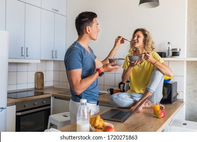 Young Attractive Couple Of Man And Woman Stay Home Together Alone Eating Breakfast Together In Morning At Kitchen, Happy Family, Romantic, Healthy Food, Cornflakes With Milk, Having Fun, Laughing