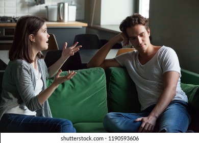 Young Attractive Couple Sitting On Couch At Home And Sorting Out Their Relations. Girlfriend Talking Too Much, Drama Queen Nagging Disinterested Boyfriend Feels Angry. Troubles And Break Up Concept