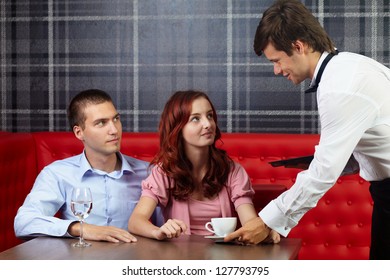 Young Attractive Couple Sitting In Restaurant And Talking To Handsome Waiter