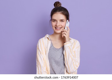 Young Attractive Dark Haired Woman With Mobile Phone Having Conversation With Friend Or Husband, Looks Happy, Having Hair Bun, Girl Wearing Casual Attire.