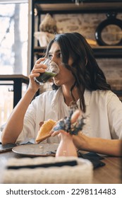 A young attractive dark-haired woman is drinking green matcha tea in a cafe.Healthy eating concept. - Shutterstock ID 2298114483