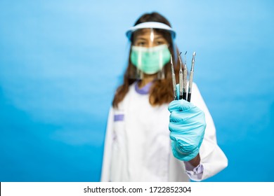 Young Attractive Dentist Wearing Surgical Mask And Face Shield. The Written On Her Gown Is He Name In Thai Alphabets