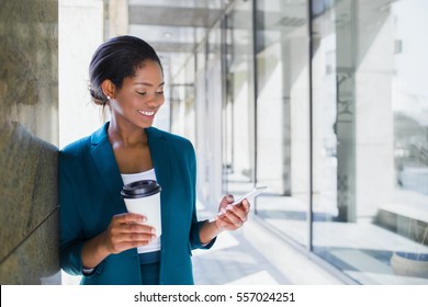 Junge attraktive, feine afrikanisch-amerikanische Geschäftsfrau in formaler Kleidung per Telefon und hält während der Pause im Büro-Saal eine Kaffee-Tasse