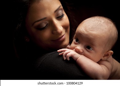 Young Attractive Ethnic Woman Holding Her Newborn Baby Under Dramatic Lighting.