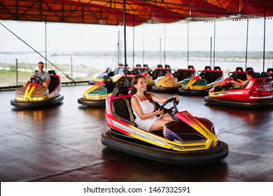 Young attractive european couple in amusement park. Male and female on romantic date in valentine's day. Boy and girl drive a bumper cars and laugh.