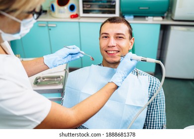A young, attractive European-looking guy came to the dentist. Sits in a dental chair. The dentist bent over him and prepares to treat problem teeth. Happy patient and dentist concept.