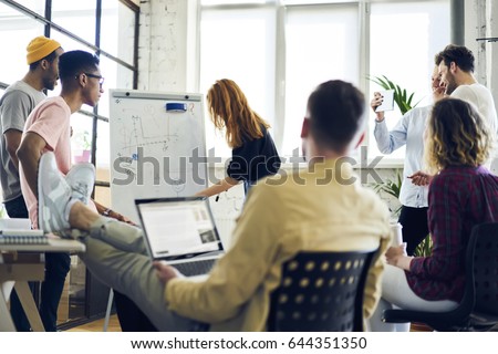 Young attractive female employee making presentation of her project for advertising campaign writing on whiteboard, young hipster girl noting on flipchart suggestion during brainstorming session
