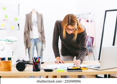 Young attractive female fashion designer leaning on office desk, working with a laptop at home