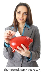 young attractive female puts 20 pound note into red piggy bank, isolated on white