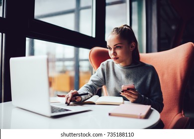 Young Attractive Female Student Searching Information For Homework Report Studying In Cafe Interior.Beautiful Freelancer Reading News From Social Networks While Doing Project For Remote Job