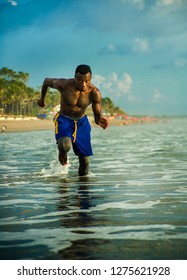 Young Attractive Fit Athletic And Strong Black African American Man Running At The Beach Training Hard And Sprinting On Sea Water In Professional Athlete Lifestyle And Ripped Runner Workout 