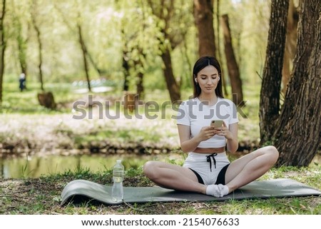 Young attractive fit caucasian sportswoman standing in nature and using smart phone to search music for running.