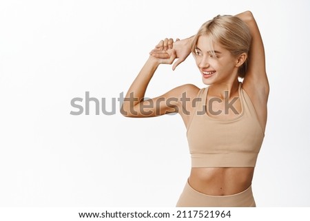 Young attractive fitness girl, female athlete stretching arms and warm up for jogging, runner doing exercises, workout in gym, showing fit strong body and biceps, white background