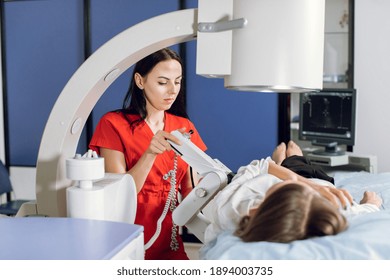 Young attractive focused woman doctor in red uniform, providing lithotripsy procedure for her lying female patient with modern ultrasonic lithotriptor to break up stones