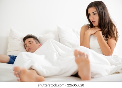 Young attractive girl after waking up in bed, looking with surprise erection her boyfriend who still sleeps covered with a sheet.
