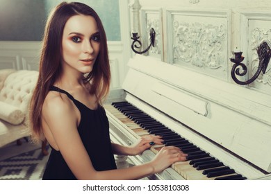 Young attractive girl in a black dress posing near an old piano
