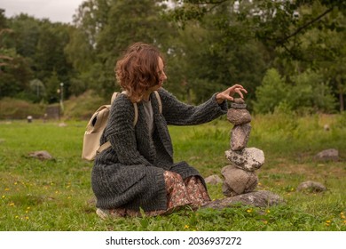 A young attractive girl builds a tower of stones. She tries to find a balance so that the stones do not fall. Overall plan from the side.