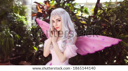 Young attractive girl dressed as fairy in green garden with pink wings