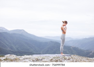 Young attractive girl standing on the peak of a mountain. Practicing yoga on a yoga mat. Surya Namaskar or Salutation to the Sun
