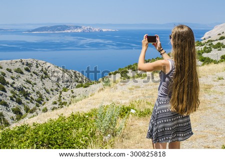 Young attractive girl taking photo of tropical landscape