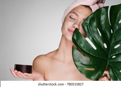 young attractive girl with a towel on her head, put on her face a coffee scrub, holds a green leaf