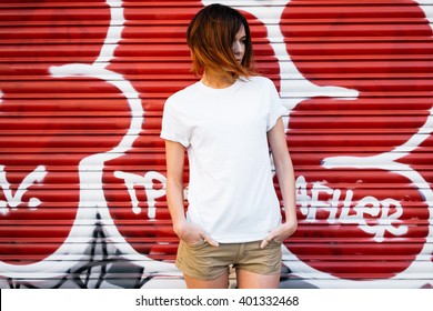young attractive girl wearing a white t-shirt standing on a graffiti wall background 