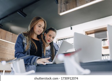 Young Attractive Girls In An Electronics Store Use A Laptop At An Exhibition. Concept Of Buying Gadgets And Going To An Electronics Store.