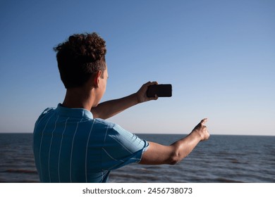 A young attractive guy is posing while relaxing on the sea and taking a photo with his phone.