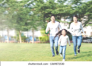 Young Attractive Happy Asian Family Playing By Running Together In Outside Nature Park In Home School Learning Or Montessori Concept With White And Blue Casual Wearing. Asian Lifestyle Parenting.