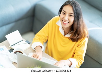 Young attractive happy asian female student sitting at living room floor smiling and looking up at camera working on laptop at home office. Young startup entrepreneur or freelance business concept.