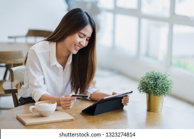 Young attractive happy Asian woman is using tablet for shopping and paying online by debit or credit cards, online purchases content, commerce on the Internet shop background with copy space.