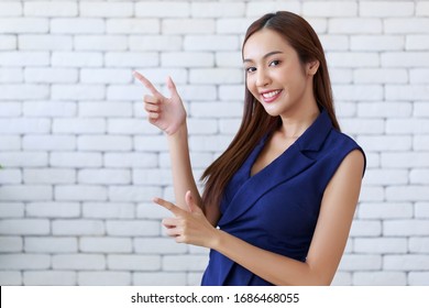 Young attractive happy Asian woman gesturing pointing at copy space, standing position at the office.