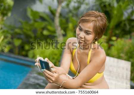 young attractive and happy Asian woman in bikini using social media internet app on mobile phone relaxed at resort swimming pool in communication and holiday vacation relax concept