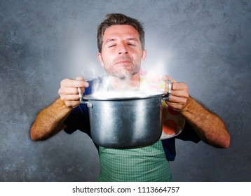 Young Attractive Happy And Proud Home Cook Man Cooking Soup Holding Kitchen Pot Smelling The Meal Aroma Gesturing Delighted And Satisfied On Isolated Background In Domestic Lifestyle