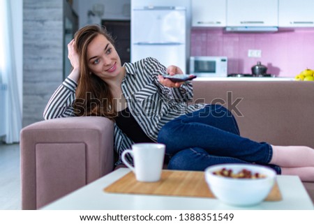 Young, attractive, happy woman resting on the sofa and watching TV at home