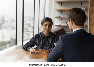 Young attractive Indian ethnicity female applicant pass job interview sits in front of male HR manager answers questions, apply for company position. Hiring agency, headhunting and staffing concept
