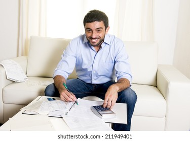 Young Attractive Latin American Business Man At Home Sitting On Sofa With Credit Card And Calculator Accounting Costs, Charges, Taxes And Mortgage For Paying Bills Looking Happy And Relaxed 